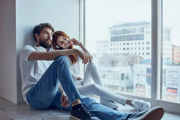 Um jovem casal sentar perto da janela com fones de ouvido juntos apartamentos — Fotografia de Stock