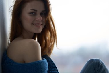 Pencerenin yanında oturan mavi ekoseli, rüya gibi bakışlı kadın.