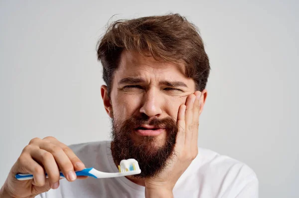 Vousatý muž zubní kartáček v ruce hygiena čisté zuby světlo na pozadí — Stock fotografie
