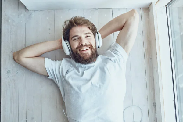 Man met baard liggend in de buurt van het raam met hoofdtelefoon Lifestyle — Stockfoto