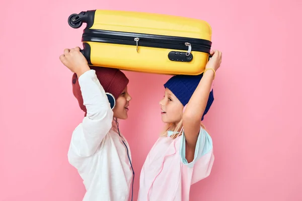 Drôle petit garçon et fille avec une valise jaune dans ses mains fond de couleur rose — Photo