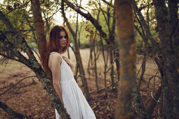 Pretty woman in white dress leaning on a tree in the summer forest. High quality photo