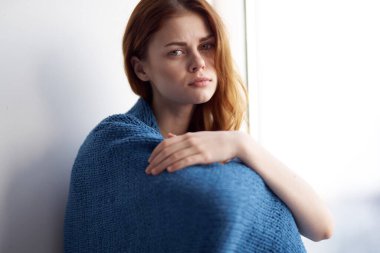 Pencerenin yanında oturan mavi ekose gülüşlü kadın.