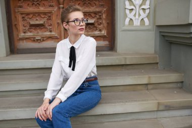 Gözlüklü güzel bir kadın elinde bir kitapla şehirde dolanıyor.