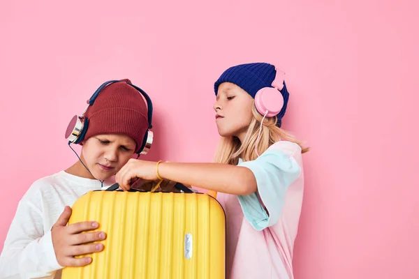 Drôle petit garçon et fille jaune valise avec écouteurs fond de couleur rose — Photo