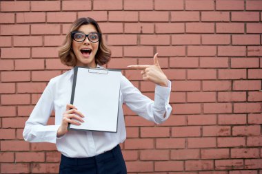 Beyaz gömlekli neşeli kadın yönetici. Tuğla arka planda belgeler var.