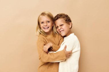 Oğlan ve kız gülümsüyor ve bej arka planda günlük kıyafetlerle poz veriyorlar.