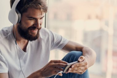 Kulaklıklı bir adam pencere kenarında oturuyor. 