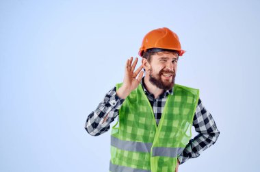 Sakallı adam yeşil yelek turuncu kask iş akışı el hareketi mavi arka plan