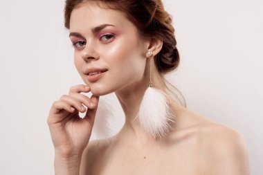 Çıplak omuzlu, parlak makyajlı, kabarık küpeli, hafif moda arka planlı bir kadın.