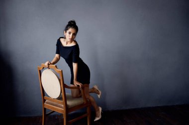 Sandalyenin yanındaki siyah elbiseli güzel kadın lüks moda yaşam tarzı stüdyosunun yanında.