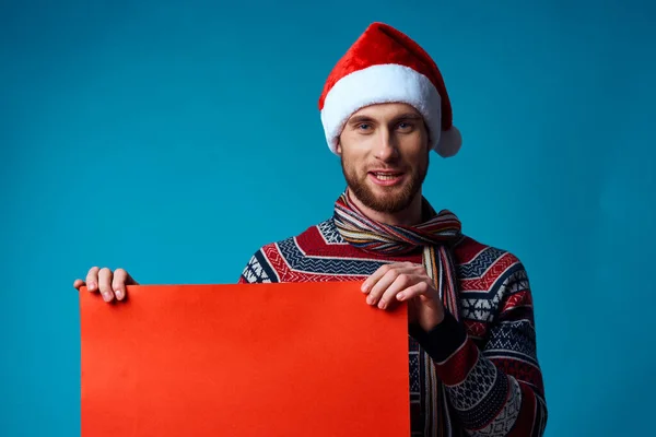 Noel Baba şapkalı duygusal adam bayramın mavi arka planını elinde tutuyor. — Stok fotoğraf