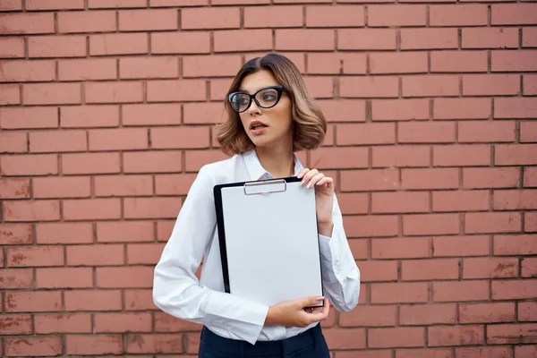 Donna d'affari in camicia bianca e occhiali con documenti sul muro di mattoni della strada — Foto Stock