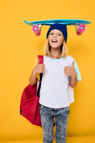 Snygg flicka glad söt barn med skateboard unge med ryggsäck gul bakgrund — Stockfoto