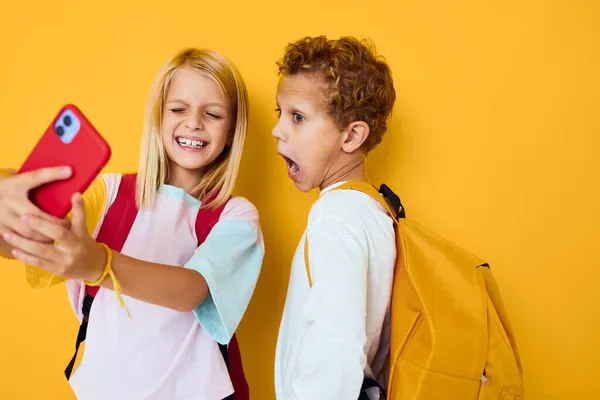 Niños de la escuela mirando el teléfono entretenimiento comunicación fondo amarillo —  Fotos de Stock