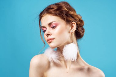 Çıplak omuzlu ve tüylü küpeli moda zevkli kozmetik ürünleri olan bir kadın.