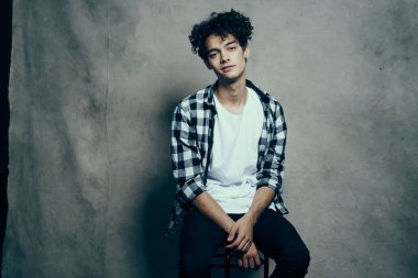 İskemlede oturan ekose gömlekli yakışıklı adam poz veriyor.