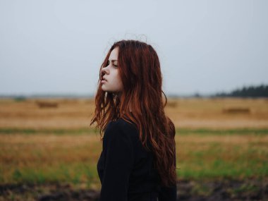 Tarlada poz veren siyah elbiseli kızıl saçlı kadın.