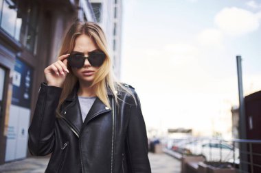 Güneş gözlüklü şık bir kadın sokakta telefonla konuşuyor.