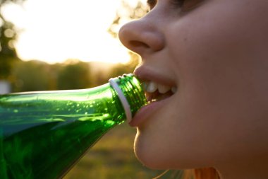 Gülümseyen kadın yeşil şişe susuzluktan su içiyor.