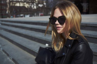 Deri ceketli kadın açık hava tatili için bina yakınında.