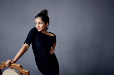 Güzel bir kadın, sandalyenin yanında duran küpeler siyah elbise yaşam tarzı stüdyosu.