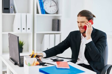 Yönetici ofisi, elinde telefon teknolojisiyle evrak işleriyle uğraşıyor.