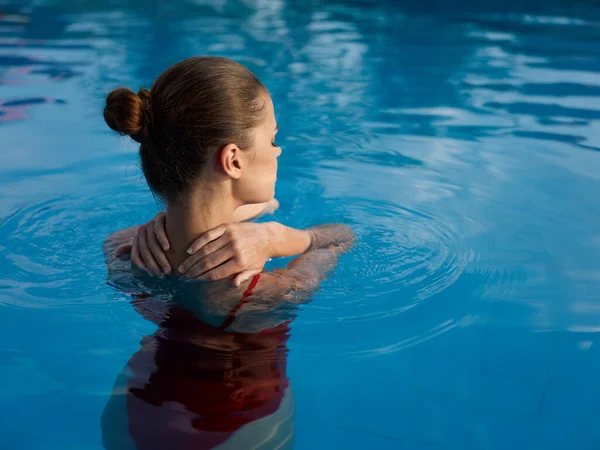 Женщина в купальнике прикасается к спине руками и стоит в бассейне в чистой воде — стоковое фото