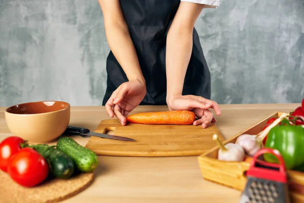 Donna in grembiule nero pranzo a casa tagliere cibo vegetariano — Foto Stock