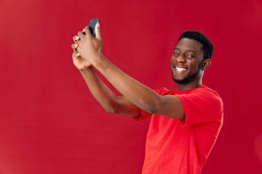 Elinde telefon olan neşeli Afrikalı adam gülümseme teknolojisi kırmızı arka plan