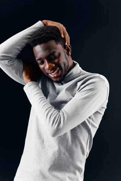 Улыбающийся мужчина африканского внешнего вида в сером свитере держа голову темным фоном — стоковое фото