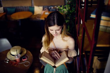 Güzel bir kadın bir kafede oturmuş bir şeyler okuyor. 