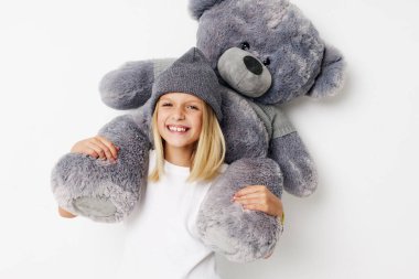 Hafif bir arka planda oyuncak ayıyla gülümseyen küçük sevimli bir kızın portresi.