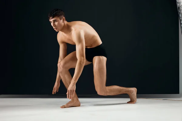 Спортсмен в чорних шортах з м'язистим тілом стоїть на темному тлі коліна — стокове фото