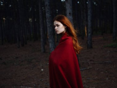 Kızıl saçlı güzel bir kadın ormanda yürüyor.