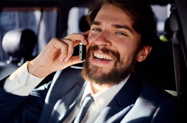 Sakallı adam araba gezisinde telefonla konuşuyor.