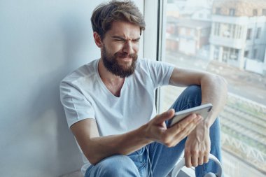 Kulaklıklı kulaklıkla pencerenin kenarında oturan bir adam.