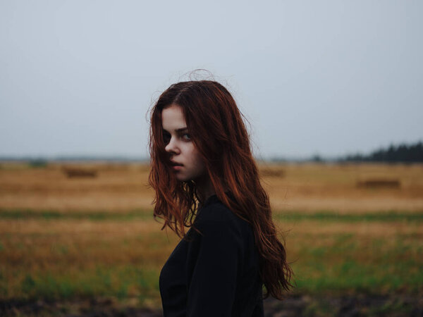Red-haired woman in black dress in a field landscape posing. High quality photo