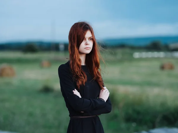 Tarlada siyah elbiseli kızıl saçlı güzel bir kadın. — Stok fotoğraf