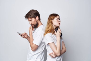 Beyaz tişörtlü bir adam ve kadın ellerinde telefonlar arka planda.