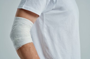 Elinde bandajlı hastane ilacı olan beyaz tişörtlü hasta bir adam.