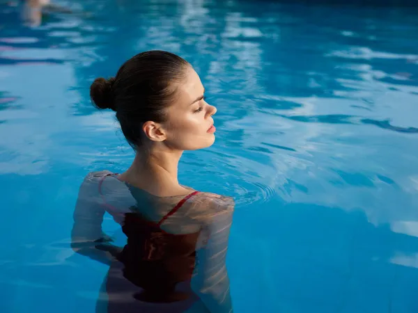 一个穿着泳衣、发型时髦的女人站在一个水边透明的游泳池里 — 图库照片
