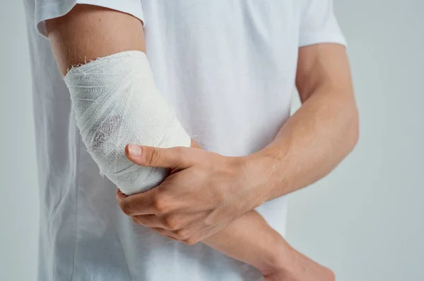 Paciente masculino con una camiseta blanca con un fondo ligero de la mano vendado —  Fotos de Stock