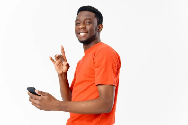 Cara feliz de aparência africana gesticulando com as mãos e segurando um telefone celular em um fundo leve — Fotografia de Stock