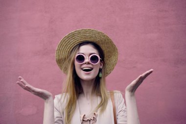 Şapkalı, gözlüklü, pembe duvarlı bir kadın.