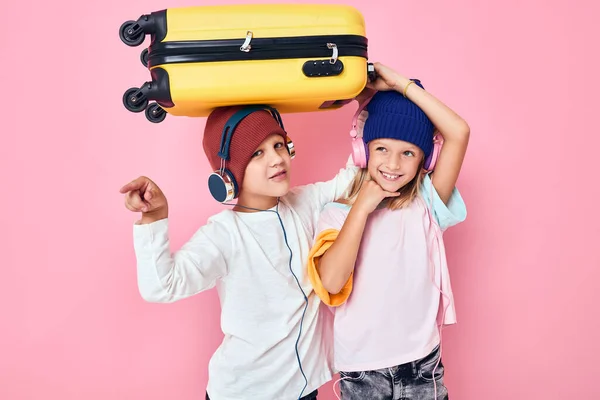Komik küçük çocuk ve kız sarı bavul kulaklık pembe arka plan — Stok fotoğraf