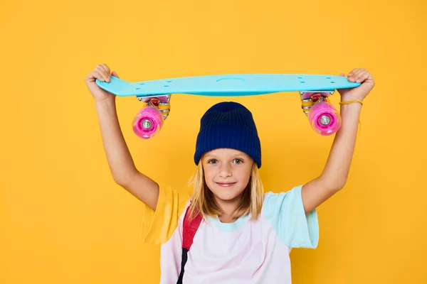 Portrét dívky s skateboardem na jeho hlavě žluté pozadí — Stock fotografie