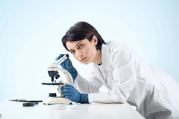 Žena lékař sedí u stolu mikroskop výzkum biotechnologie světlo pozadí — Stock fotografie