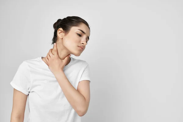 Mujer en una camiseta blanca dolor en el cuello fondo claro —  Fotos de Stock