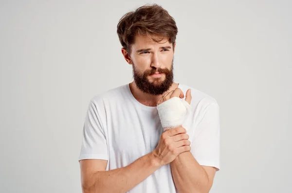 Uomo barbuto in una t-shirt bianca con una mano fasciata in posa medicina ospedaliera — Foto Stock
